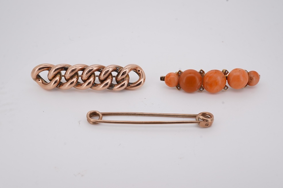 An early 20th century yellow metal and graduated five stone coral bead brooch, with seed pearl spacers, 45mm, together with a yellow metal curb link brooch and a yellow metal (stamped 9c) safety pin. Condition - fair
